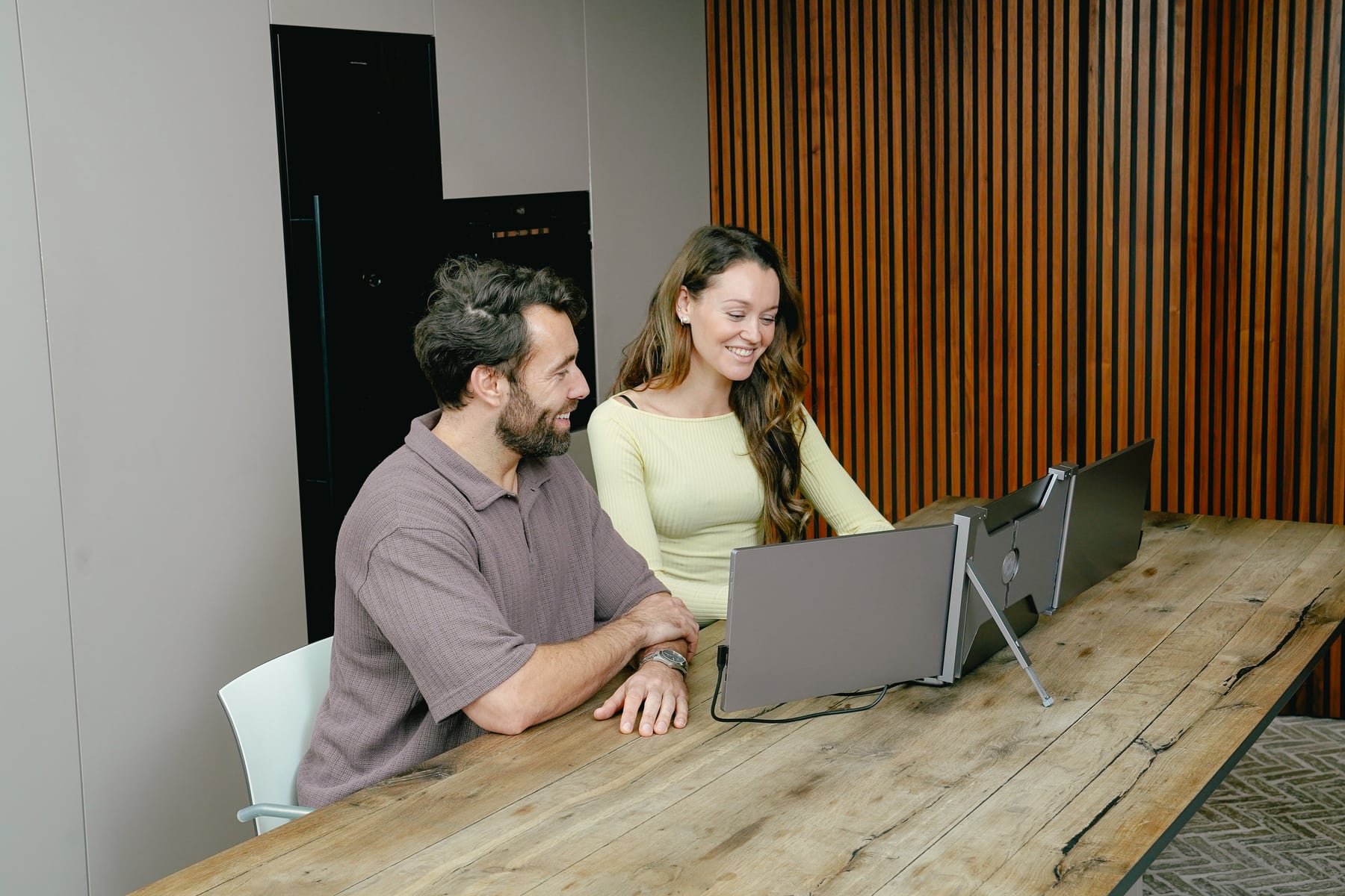 Twee mensen bekijken de achterzijde van de grijze Screenmate Expand aan tafel